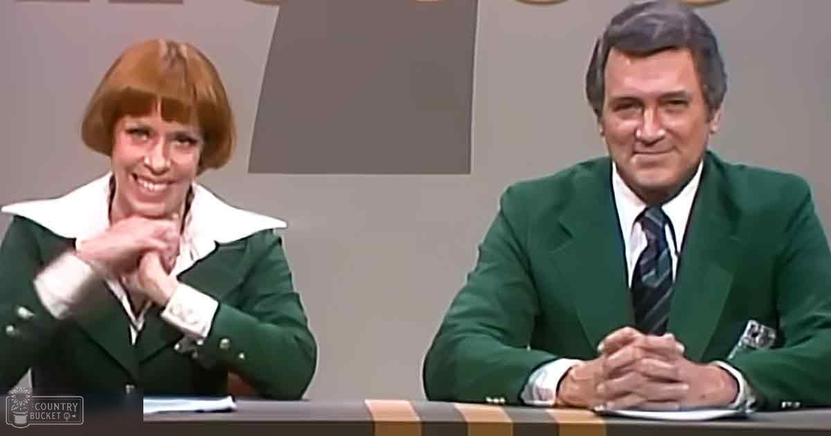 An adult male singer and an adult female guest wearing tailored green blazers with white collars, sitting at a table in a television studio set up for a talk show or news program.