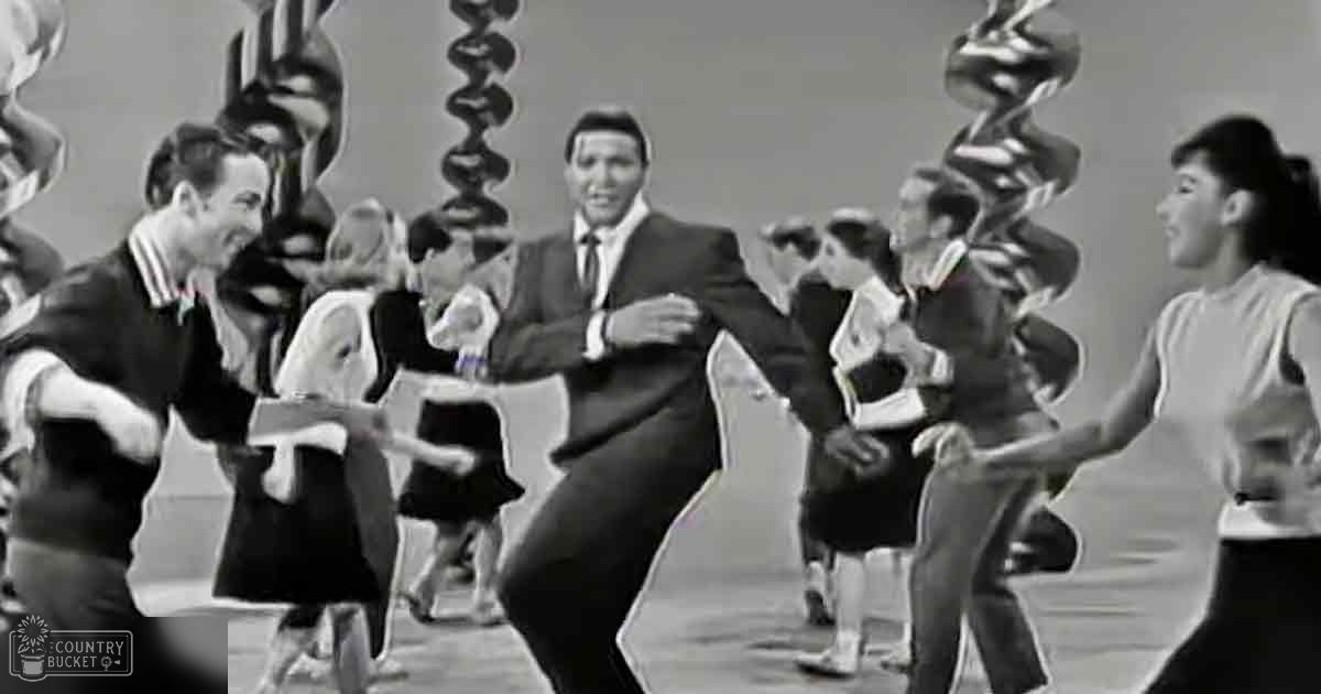 Group dance performance with mid-20th-century attire in an indoor studio setting during the daytime.