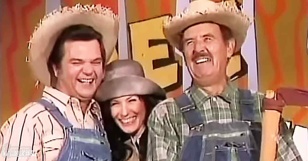 A comedic scene from a television show set against a rural backdrop with large letters spelling 'THE' with warm tones and patterns, likely an indoor farm or countryside set.