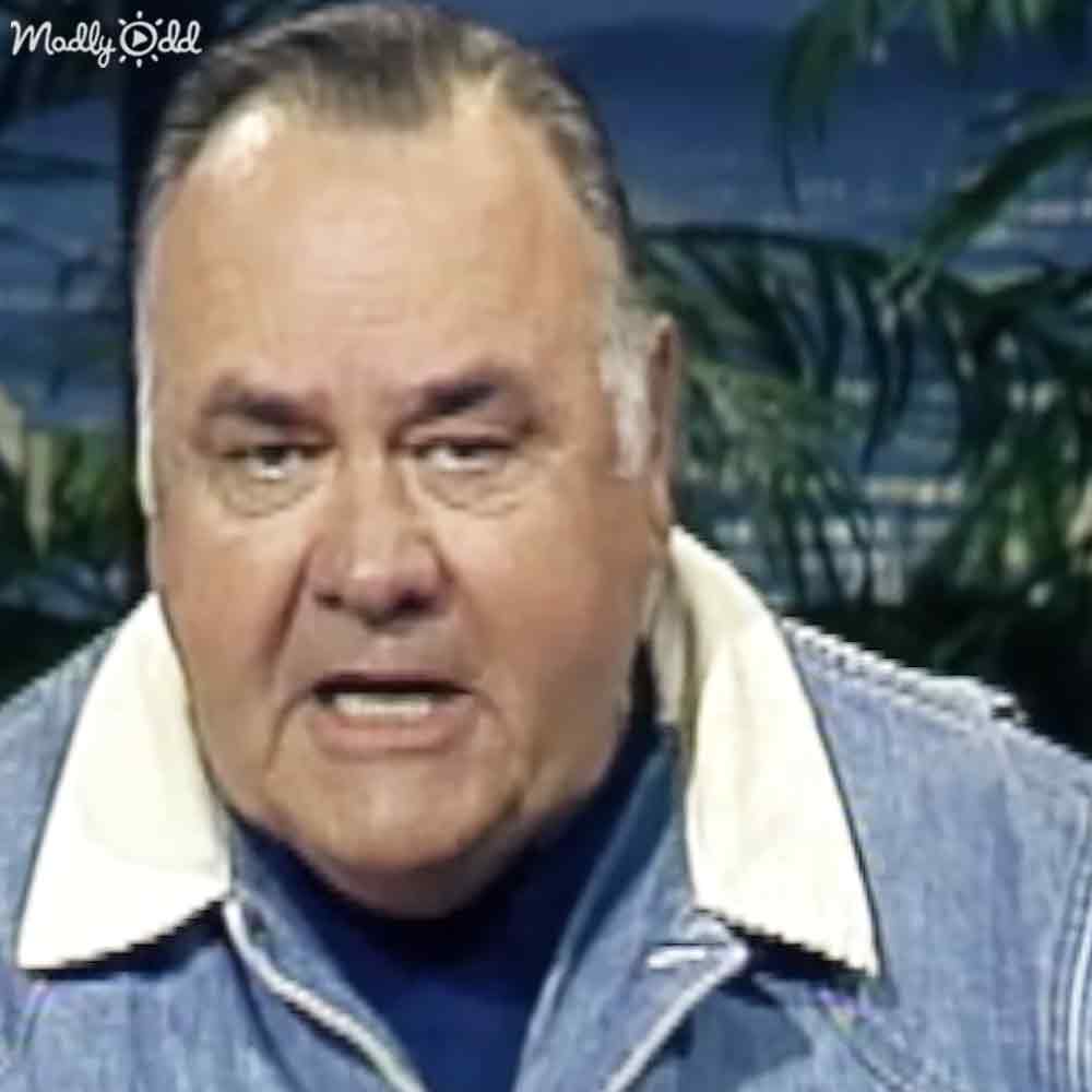 An older adult male in a tropical setting wearing a denim jacket and blue shirt, surrounded by palm trees under natural daylight.