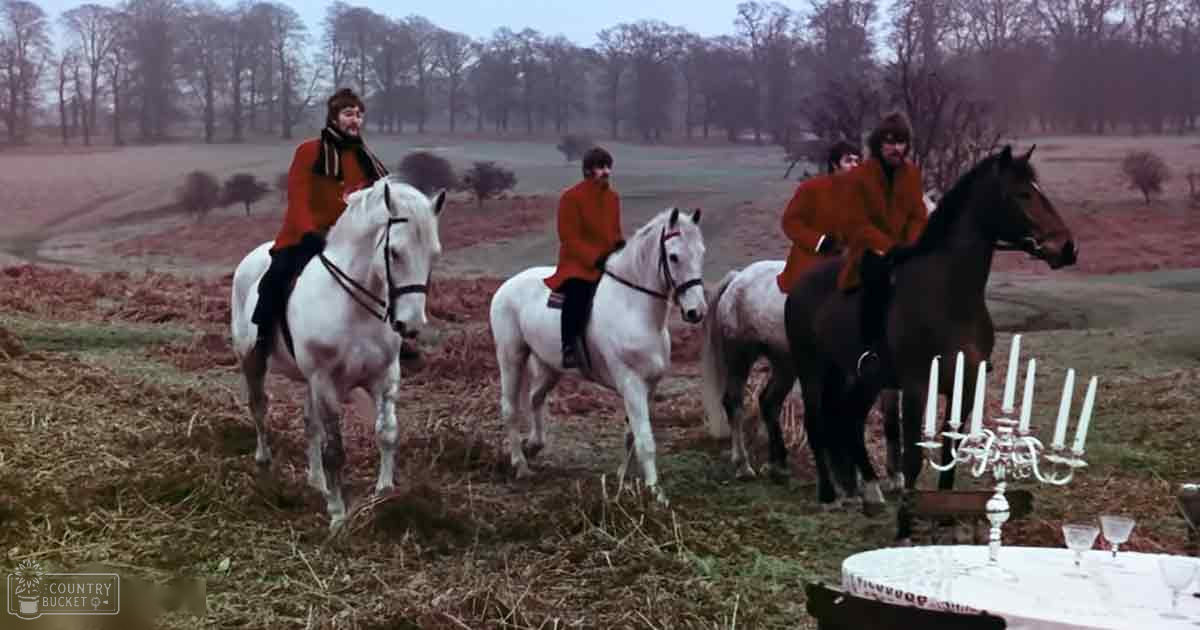 Four young men riding horses in an open field with a formal outdoor dining setup in the background.