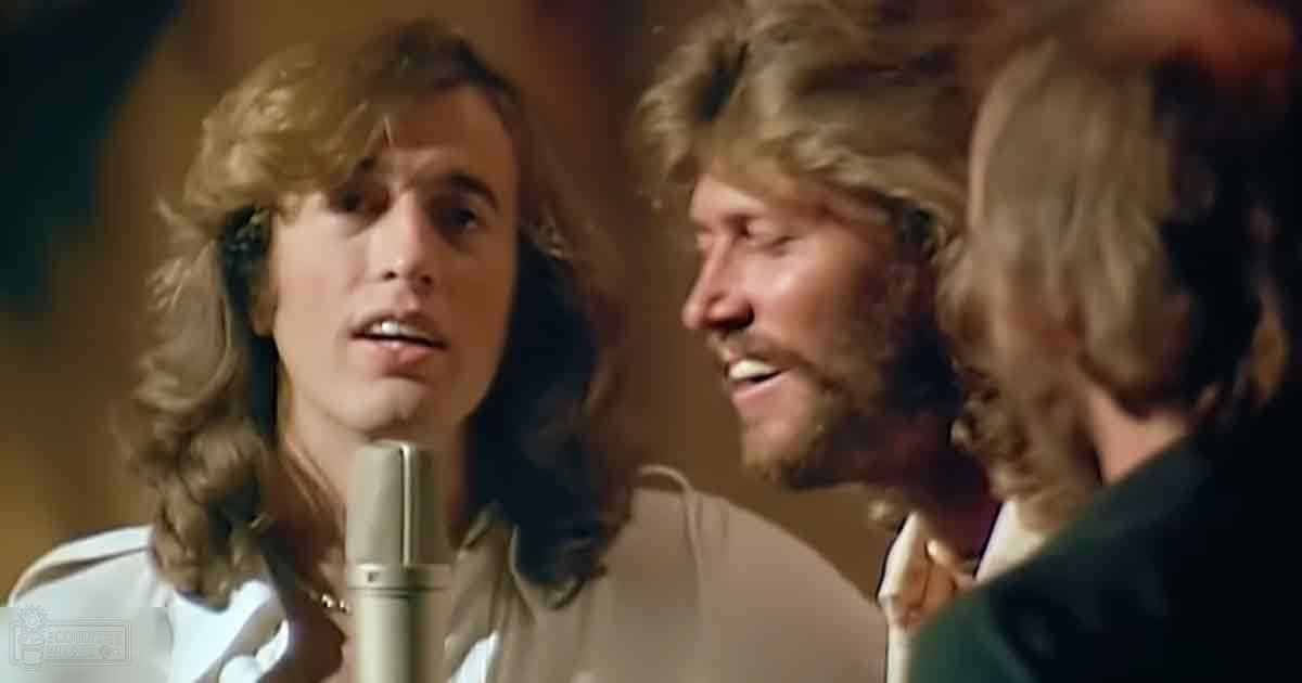 A musical performance scene with three adult males on stage under warm lighting.