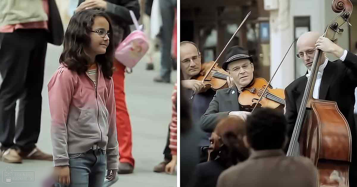 A young girl in a pink zip-up hoodie and blue jeans walks with earphones around her neck in an outdoor urban setting; two adult male musicians play the violin and cello, wearing dark suit jackets and hats under light-colored shirts.
