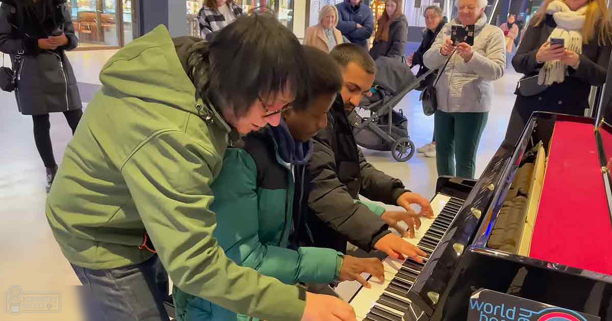 A group playing piano in what appears to be a public space, possibly a shopping mall.