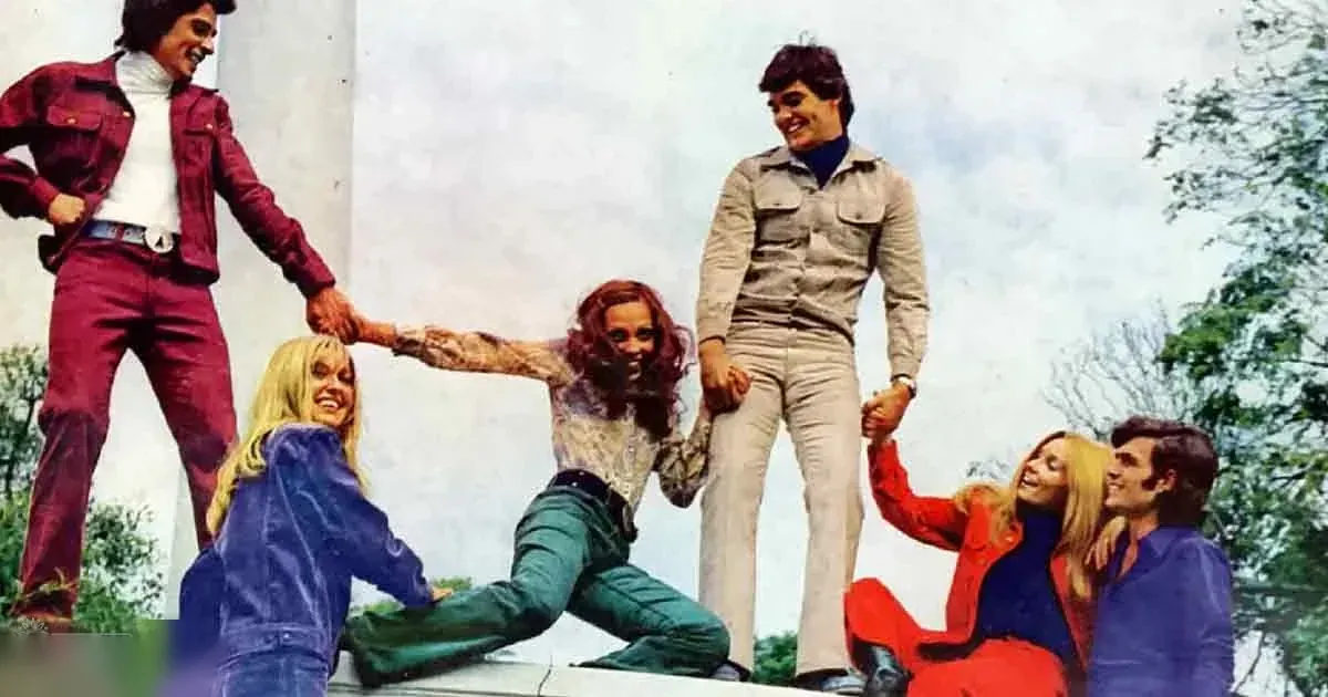 A group of young adults dressed casually outdoors with trees and a stone structure in the background.