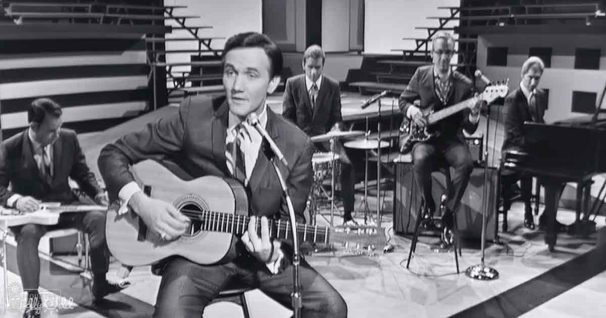 Adult males in a studio setting playing musical instruments with a grand piano, drum set, and chairs visible.