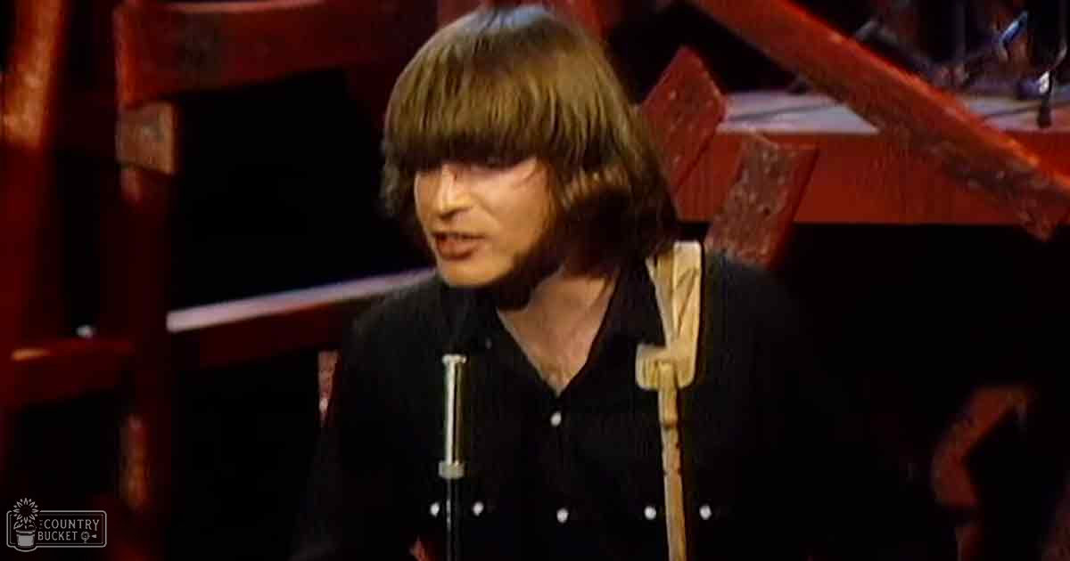 A young adult male wearing a dark button-up shirt in what appears to be a music performance setting with professional audio equipment and a red piano.
