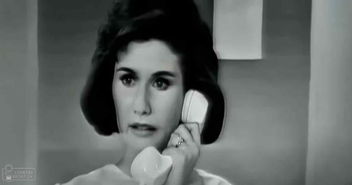 A young adult female in a mid-20th-century setting, wearing a white blouse with short sleeves and holding a telephone receiver.