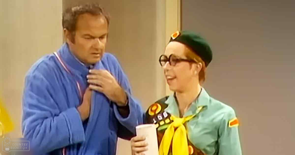 Middle-aged male in a blue robe with red and white trim, young adult female in a light teal jacket with orange accents on shoulders and yellow ribbon around her neck, set against neutral-colored walls indoors.