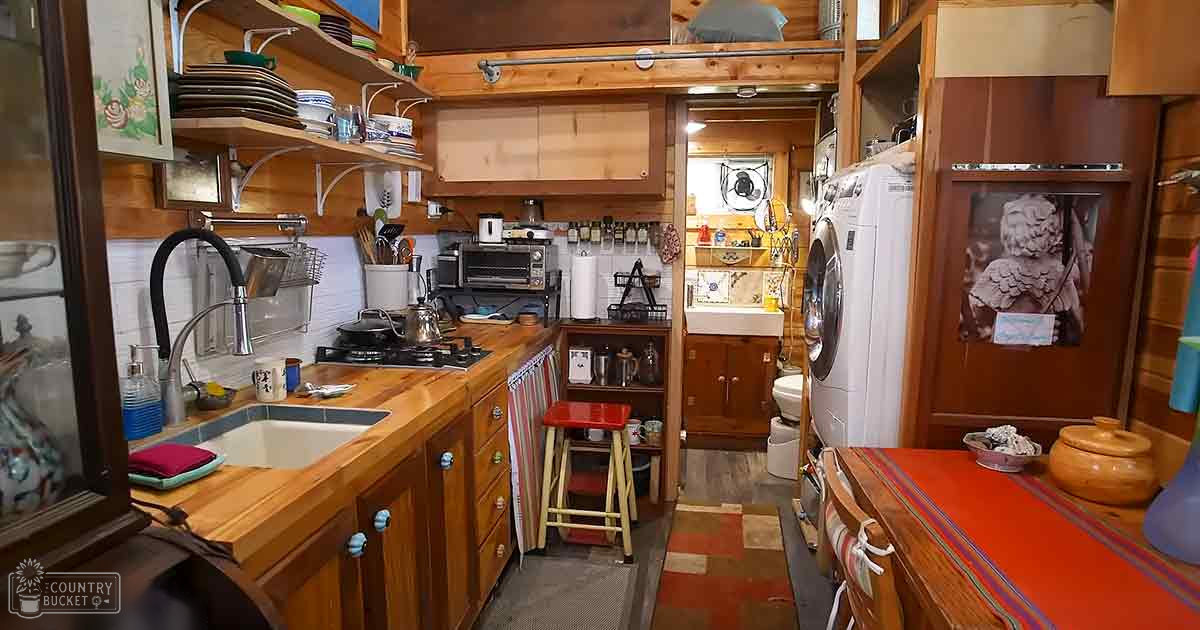 An indoor kitchen scene with wooden countertops, a sink, open shelving, and various kitchenware under natural light, suggesting daytime in a temperate climate.
