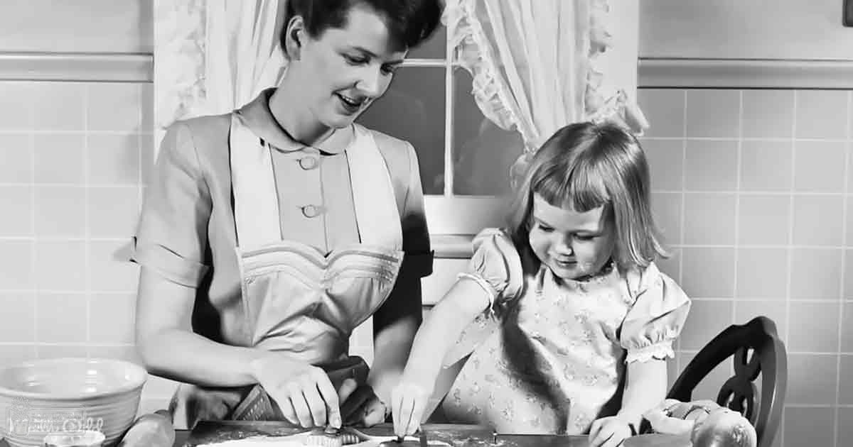 A woman in a fitted dress with puffed sleeves stands beside a toddler wearing ruffled sleeves in a kitchen setting with tiled walls and curtains, suggesting spring or summer based on attire.
