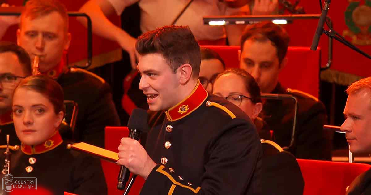 A young adult male and a female teenager in military-style uniforms are seated at an indoor event with red seating, suggesting a formal performance or ceremony.