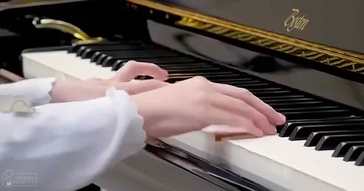A young adult female playing a grand Bösendorfer piano indoors with white ruffled sleeves and dark surroundings.