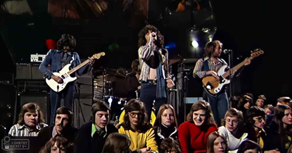 A musical performance with young adults on stage, dimly lit concert setting, audience in rows facing performers.