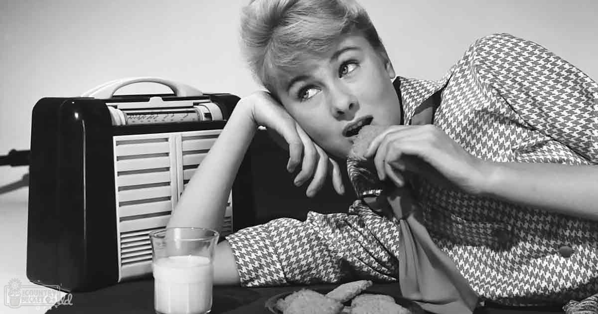A young adult female in a houndstooth-patterned dress with long sleeves, indoors in a home environment.