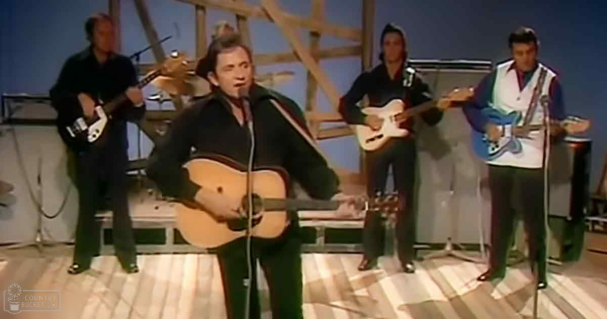 A male performer singing into a microphone while playing an acoustic guitar in what appears to be a music performance or recording studio setting.