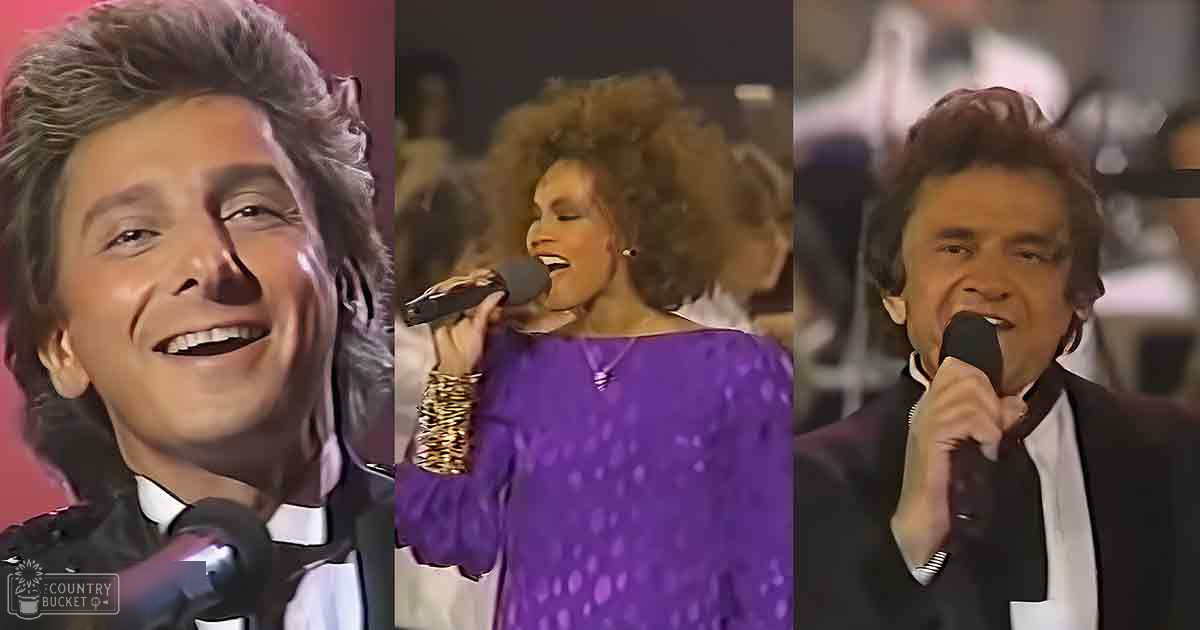 Adult male singer in a black tuxedo with white shirt and bow tie, accompanied by two adults: one in a purple dotted silk dress, another in a black wool suit jacket over a white shirt. Indoor stage lighting suggests a concert or music event at night.