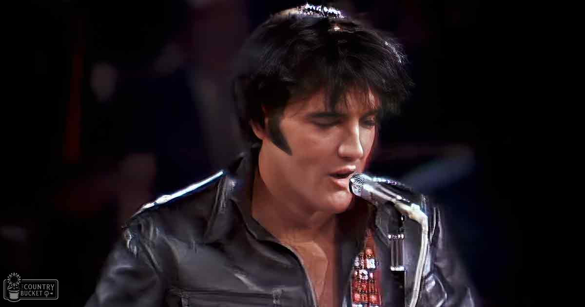 Adult male performer wearing a black leather jacket with white piping, singing or performing on an indoor stage under dramatic lighting.