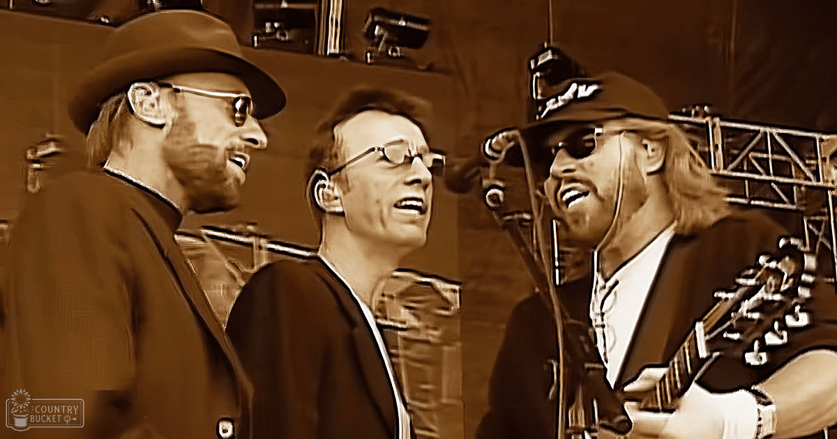 A musical performance scene in a concert setting with an adult male singer wearing a wide-brimmed hat and sunglasses on stage, accompanied by two other performers dressed formally.