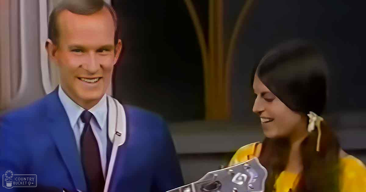 A man in a blue suit and a woman in a yellow floral top are seen together indoors, possibly at an event or studio.