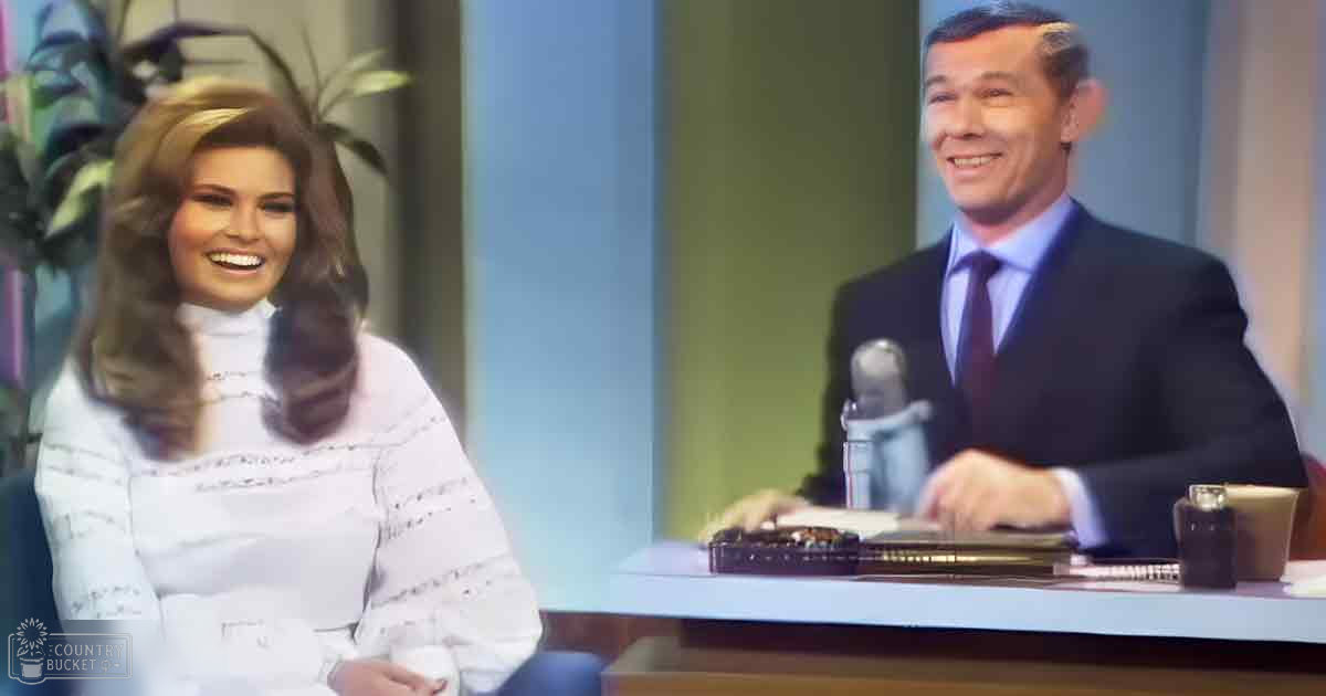 An adult female wearing a white, lace-detailed blouse seated at an interview set from mid-20th century; alongside her is a man in a dark suit with a white shirt and tie, suggesting a formal studio setting.