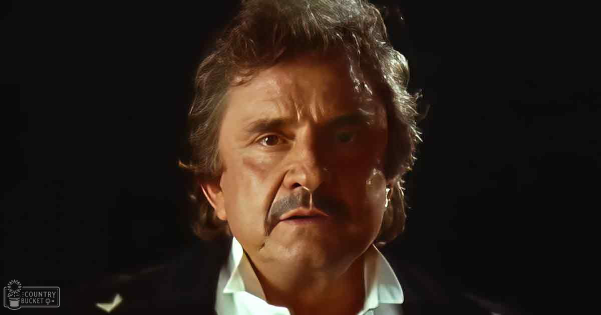 An older adult male with curly hair, wearing a white collared shirt in an indoor dark setting at night.