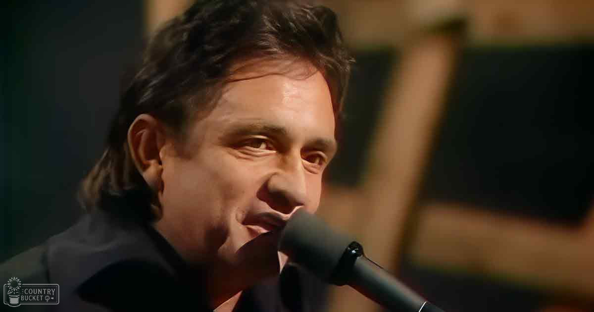A middle-aged man wearing a dark-colored, tailored suit jacket at an indoor event setting with stage lights.