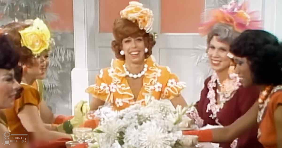 Three women in a social gathering indoors with floral dresses and accessories; light-colored walls and white flowers on the table suggest daytime event.