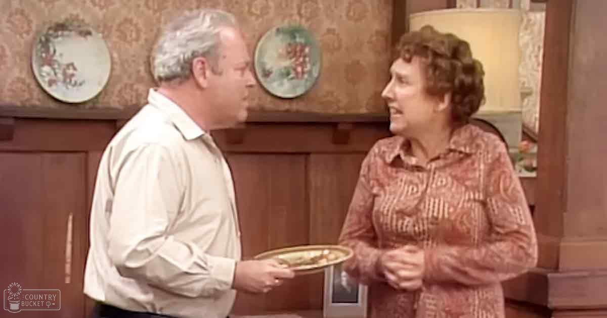 A middle-aged man holding a tray with food, interacting with an older adult woman in a home setting.