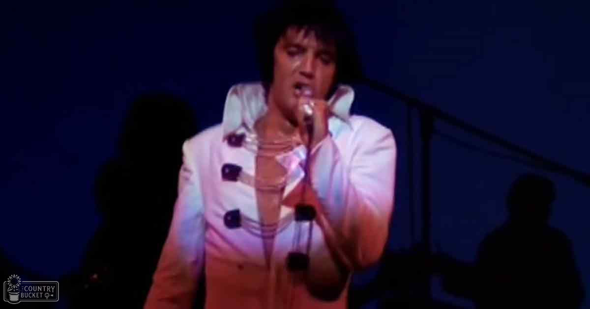 An adult male singer performing on stage at night, wearing a white button-up shirt and black buttons, possibly from mid-20th century style.