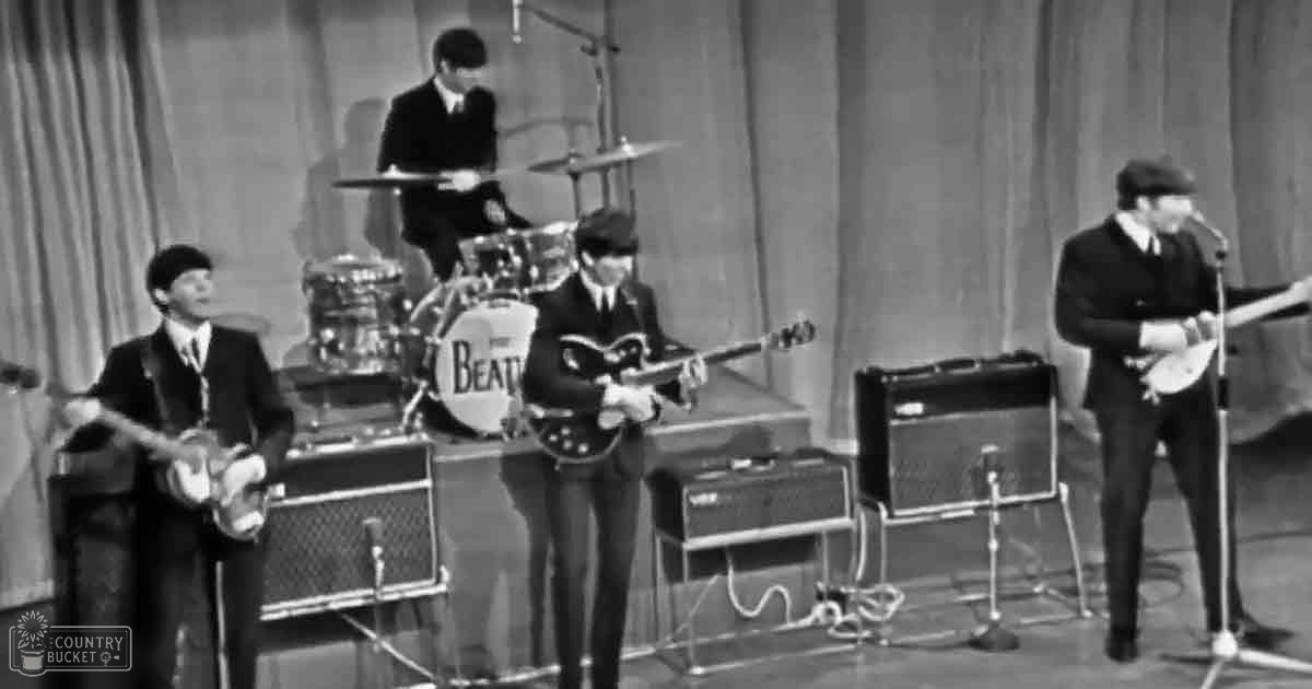 A mid-20th century studio performance of 'The Beatles' with four young adult males in dark suits against a backdrop of curtains and musical equipment, black-and-white aesthetic typical of the era.