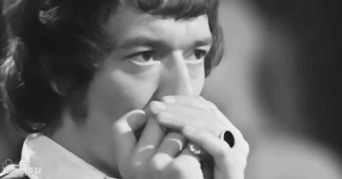 A young adult female wearing a loose-fitting, collared white blouse with long sleeves in an indoor setting with soft, even lighting and black-and-white monochromatic tones.