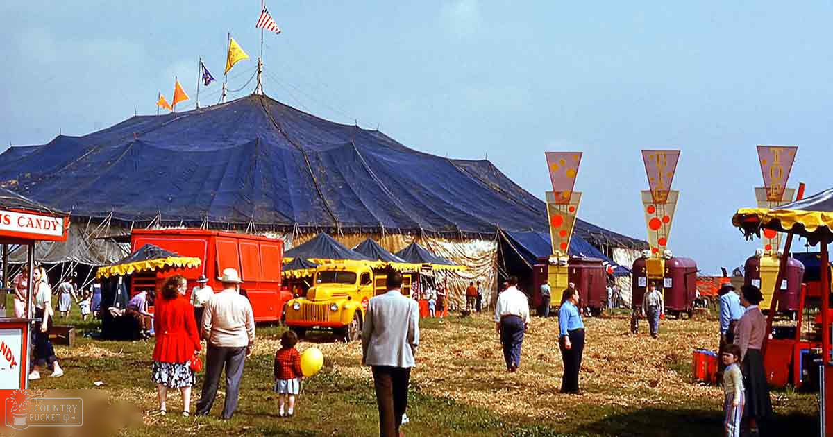 A child in a red polka-dotted dress and toddler with white shoes at an outdoor fairground with red trucks and 'CANDY' signs.