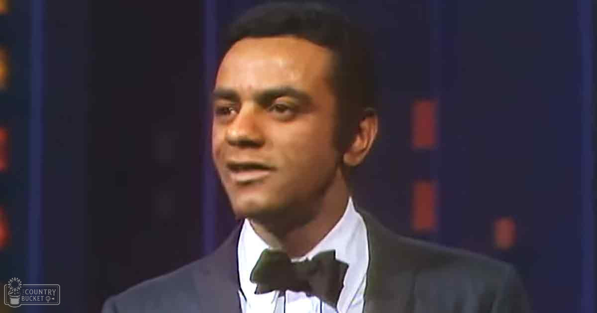 A young adult male in a formal suit with bow tie stands indoors against a stage-like background.