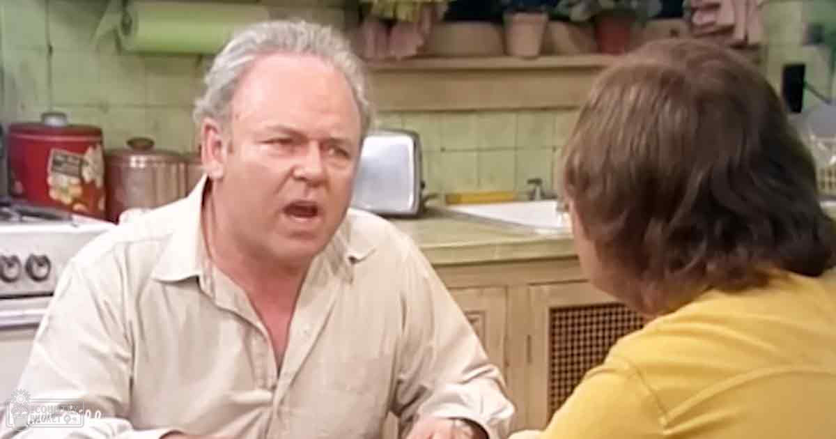 Middle-aged man with gray hair in a light-colored button-up shirt, standing beside a child wearing a yellow t-shirt in a home kitchen setting.