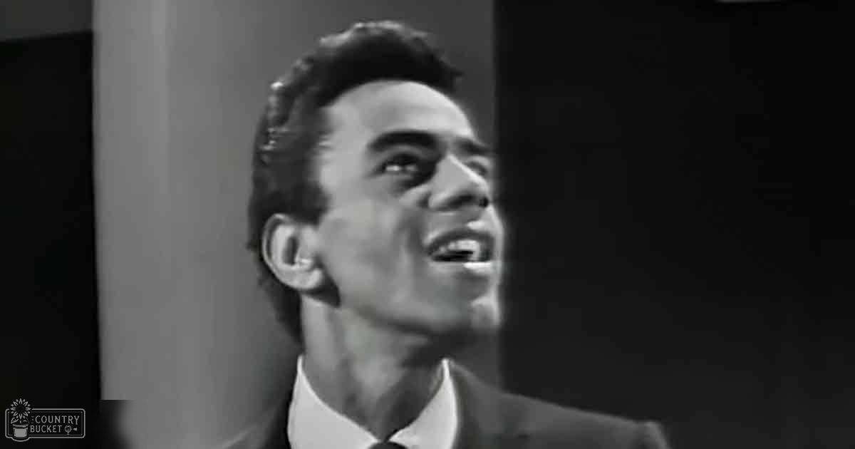 A young adult male in a dark suit jacket and white shirt indoors with dramatic lighting.