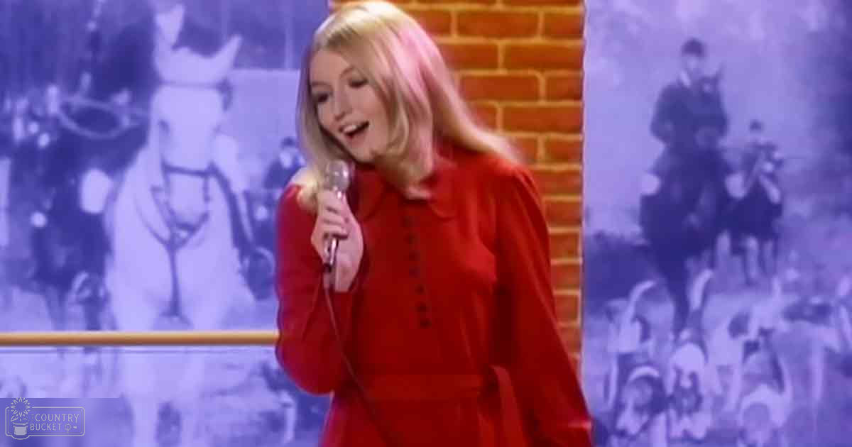 A young adult female in a red, button-down dress sings into a microphone against a backdrop with a mural of people and horses.
