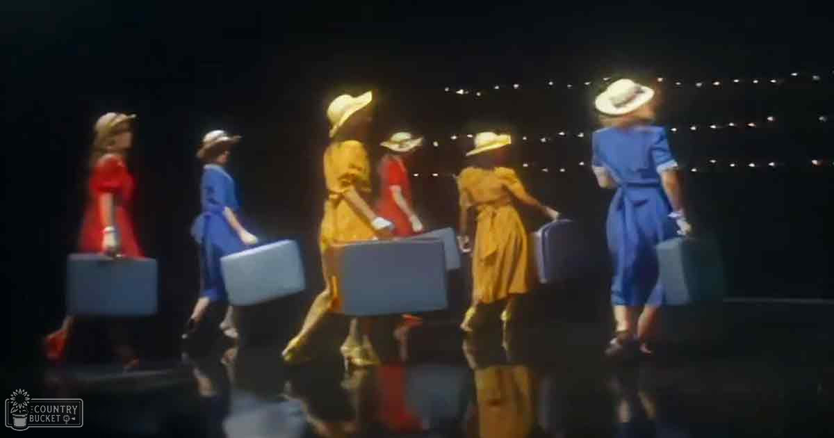 A group of women in vintage attire at an airport or train station under string lights at night.