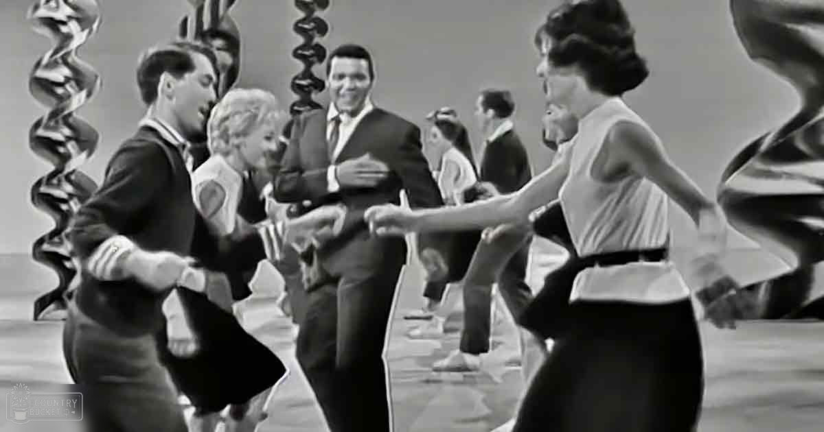 A dance scene in an indoor setting with young adults performing on a stage decorated with columns and sculptural elements.