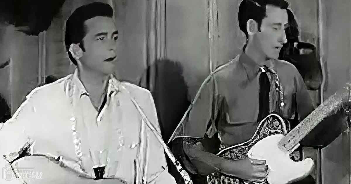 A mid-20th century musical performance scene with two adult male singers on a stage holding an electric guitar, set against curtains and faint audience members.