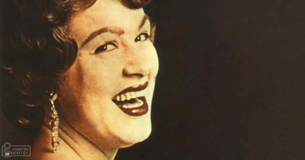 A middle-aged female with dangling earrings and red lipstick in a dark indoor setting.
