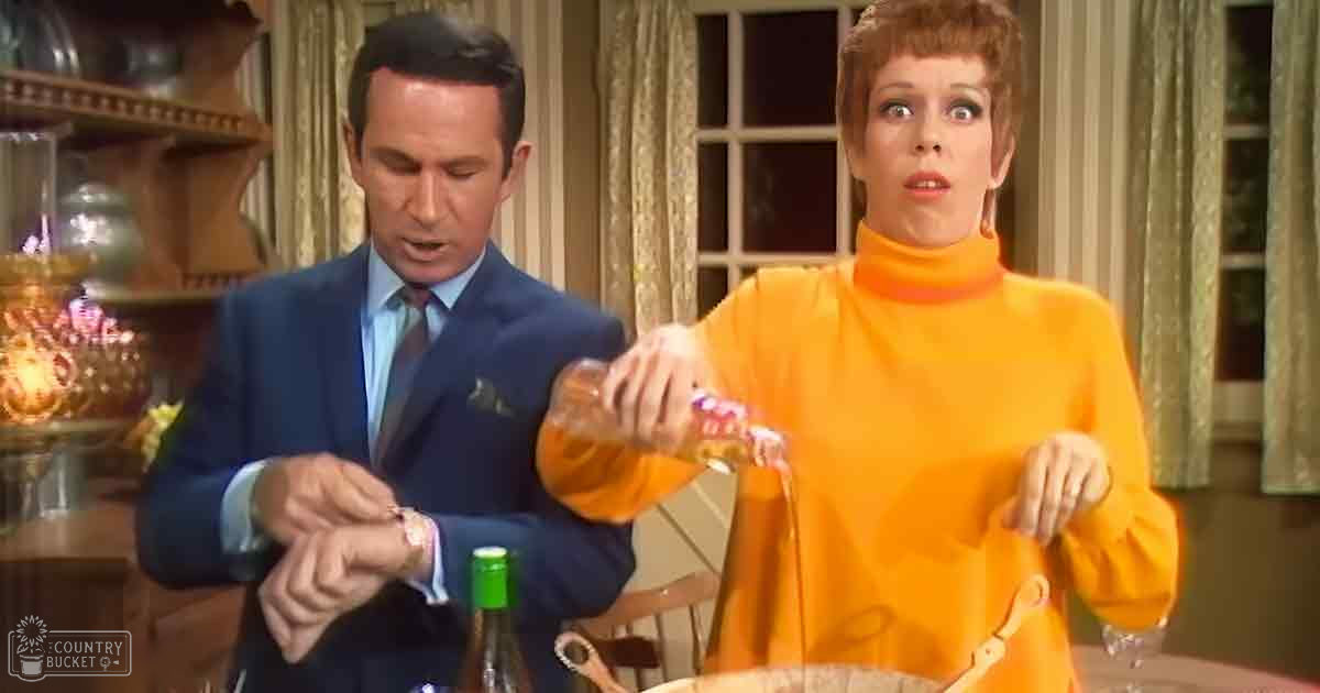 Indoor scene with two adults, one in a dark blue suit and the other in an orange turtleneck sweater. Curtains suggest daytime light.