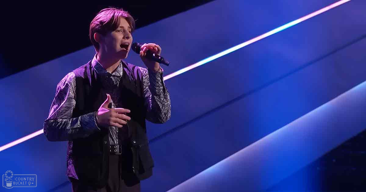 A young adult male singer performing on a stage with dynamic blue and purple lighting, wearing a patterned shirt layered under a dark vest.