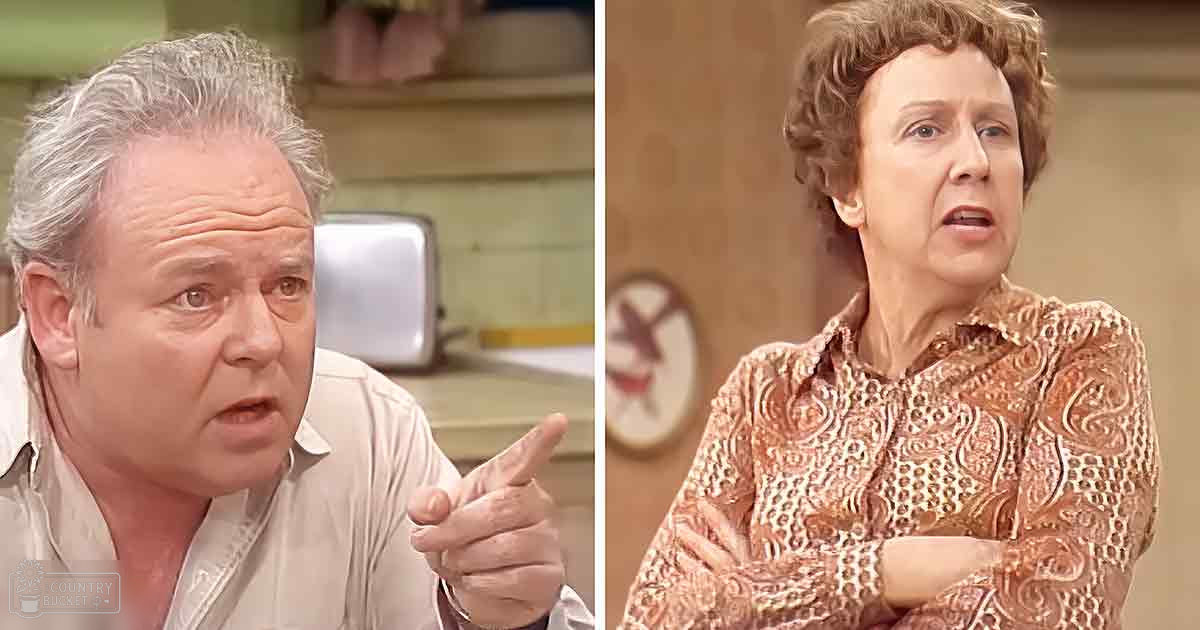 Middle-aged male in a light beige button-up shirt with pocket detail stands beside an older adult female wearing a patterned blouse in shades of pink and brown, both indoors in what appears to be a kitchen setting.