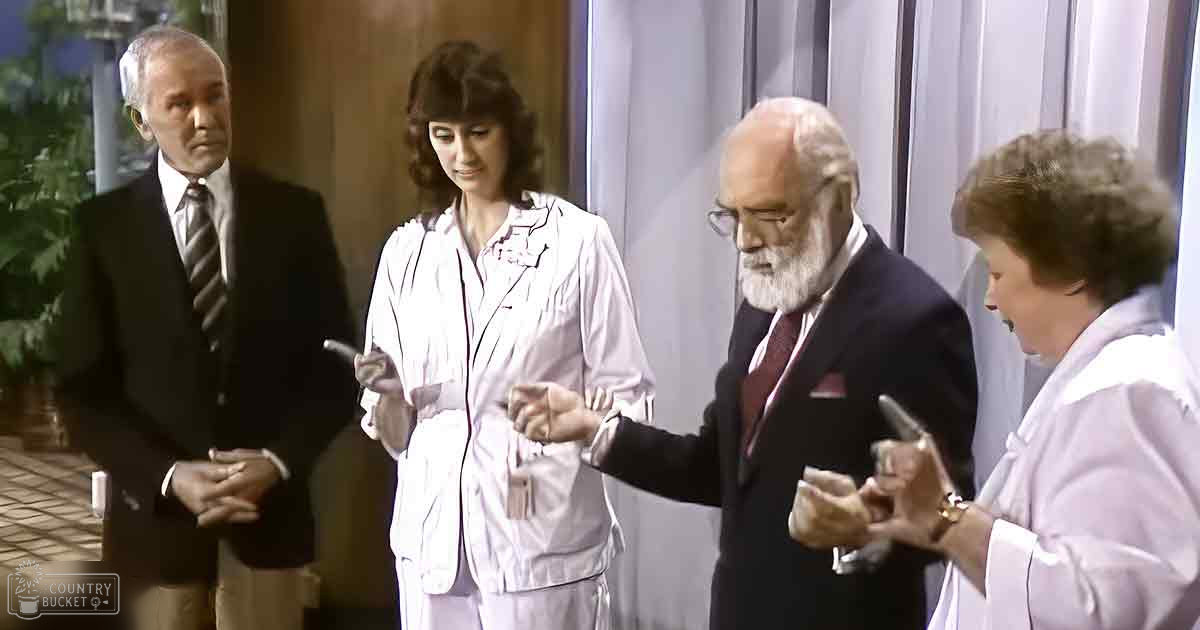 Four adults dressed formally and casually, possibly scientists or professionals, gathered in what appears to be a laboratory setting with typical office furniture.