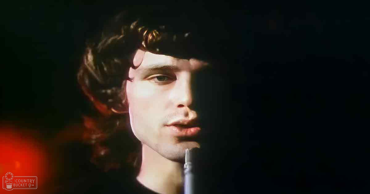 A young adult male wearing a dark-colored shirt stands in front of a microphone, likely during a performance or recording session with dim red lighting and dark tones dominating the scene.