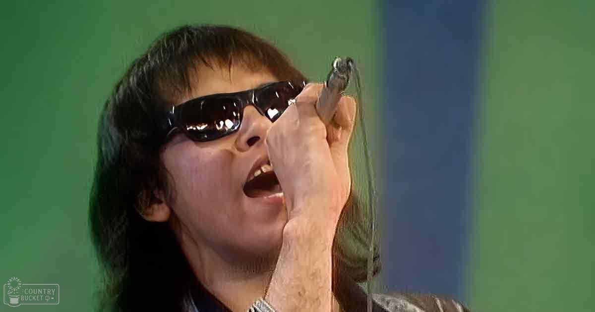 Young adult male wearing a tight-fitting leather jacket with high collar, dark brown color, likely modern classic rock style.