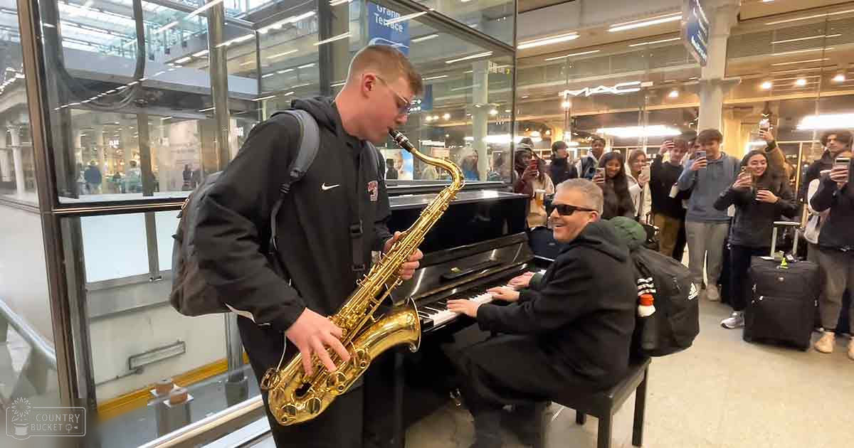 A saxophonist playing amidst an audience and luggage in a well-lit train station setting.
