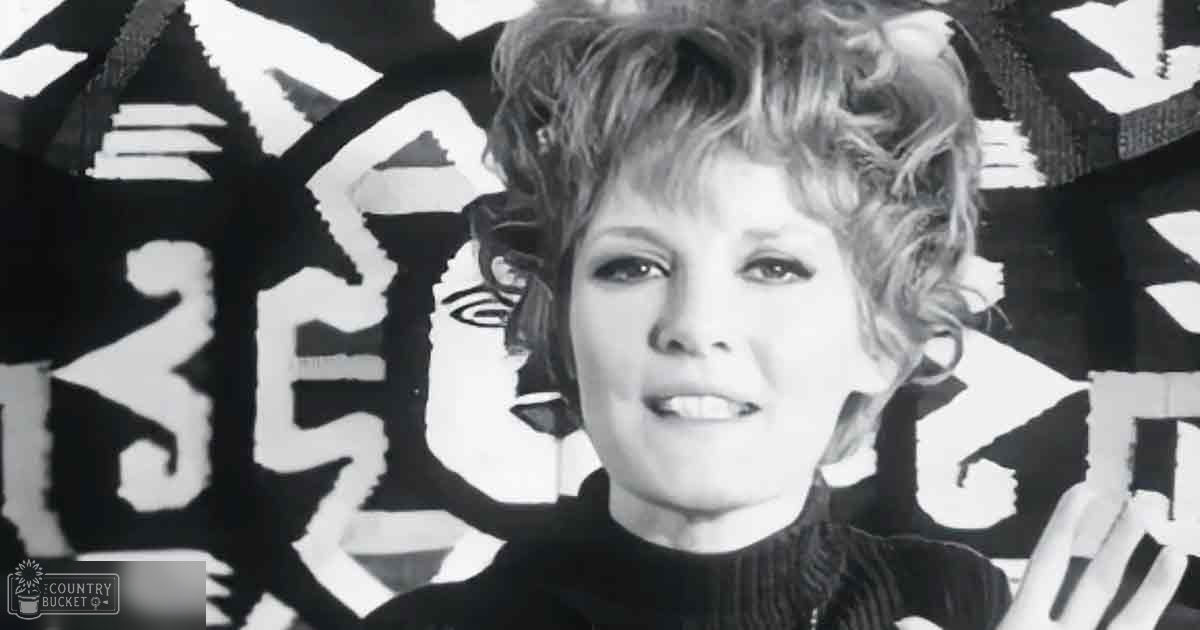 Middle-aged adult female wearing fitted black turtleneck sweater with vertical ribbed texture in an indoor setting with abstract black-and-white artwork with bold geometric shapes and lines.