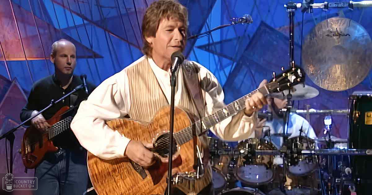 Middle-aged man playing guitar on a stage with geometric shapes and microphones around him.